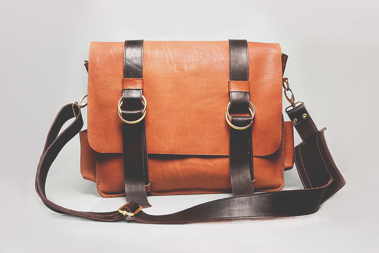 about-us-01 Elegant brown leather briefcase with dark straps and metal buckles, ideal for fashion and business.